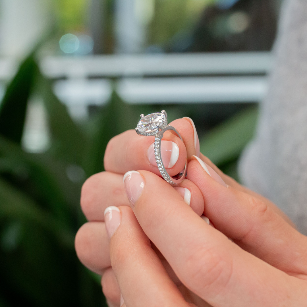 A close-up of a person holding an engagement ring with a diamond and a band decorated with smaller diamonds.