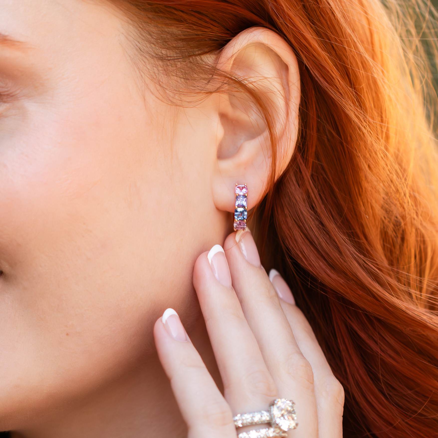woman with diamond ring and band on her hand and multi-colored stone huggie earring