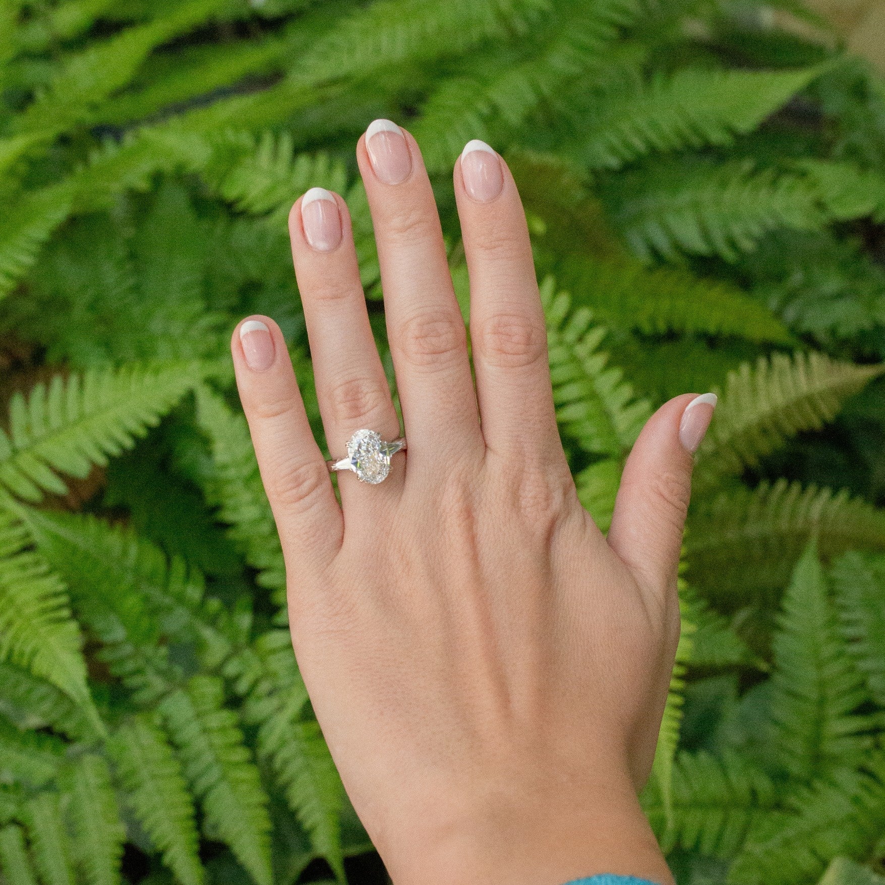 Womans left hand with diamond ring and trees in background