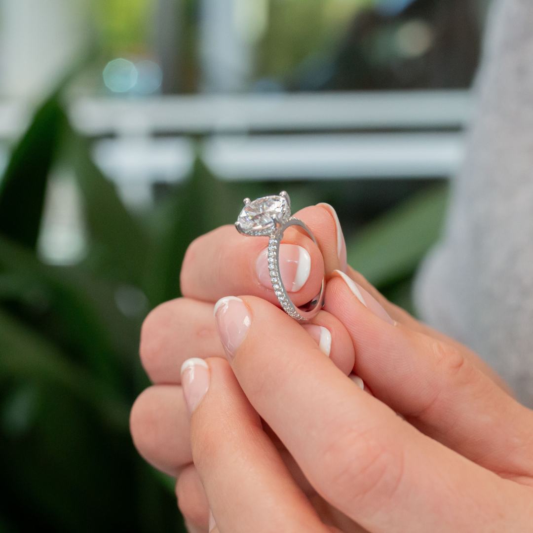 A close-up of a person holding an engagement ring with a diamond and a band decorated with smaller diamonds. 