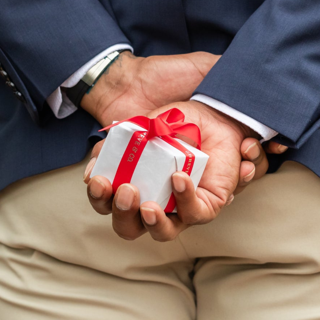 man holding a box with red ribbon behind his back.