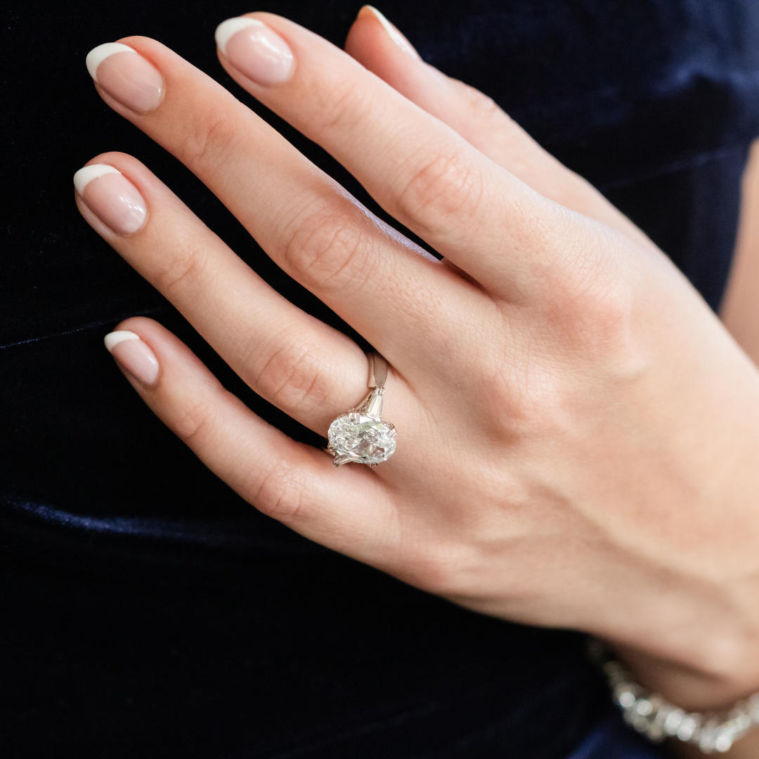 a woman wearing a large oval engagement ring on her ring finger with manicured fingers